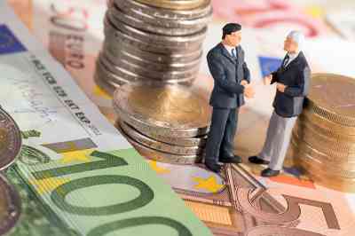 Zwei kleine Figuren stehend auf Geldscheine umringt von Münzen  - © PhotographyByMK - stock.adobe.com